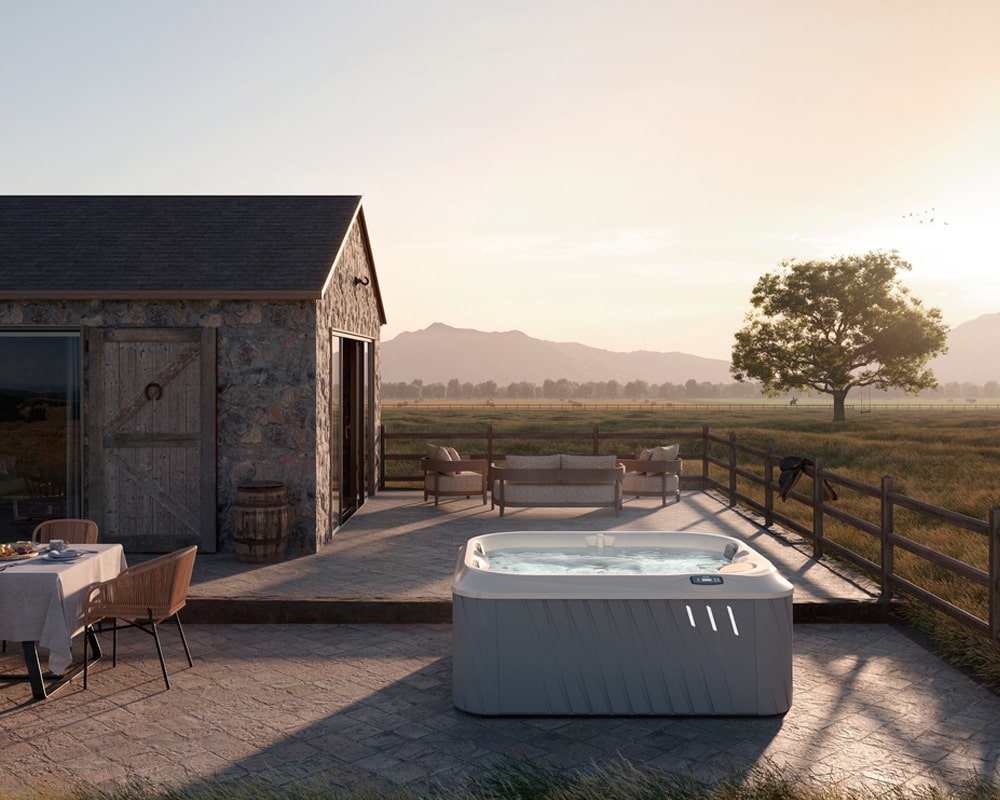 JHT J-225 hot tub on a paved patio, and a dining table, all overlooking a peaceful countryside landscape