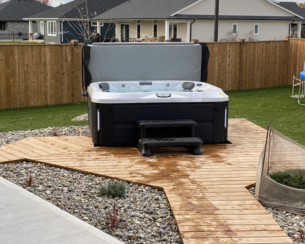 Modern outdoor hot tub with a cover, placed on a wooden path surrounded by gravel and grass